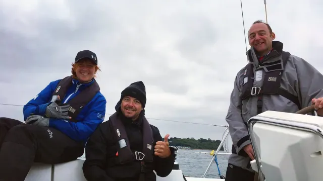 Sailing school students smiling together on deck, one at the helm of a yacht