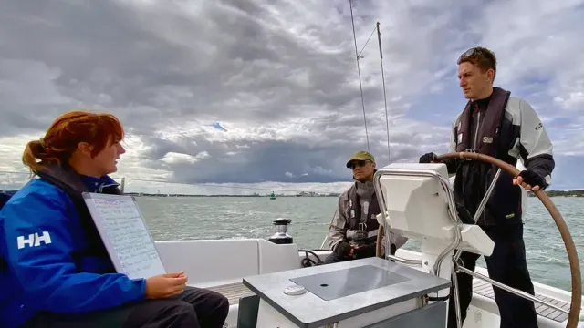 Sailing school students practising helming a yacht while making notes on a whiteboard