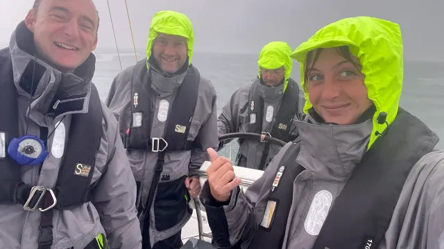 Sailing school students helming a yacht in heavy rain wearing grey and neon yellow foul-weather gear
