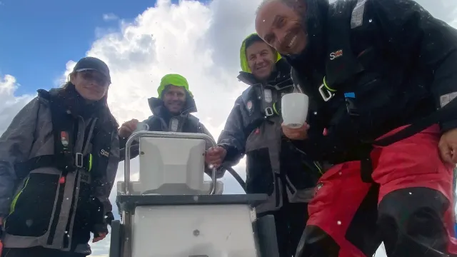 Crew members at the helm of a sailing school yacht in wet weather gear