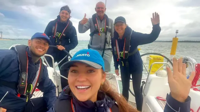 Sailing school students and instructor smiling and waving on deck during a training sail