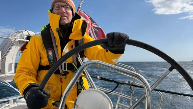 Sailing school student in yellow foul-weather gear steering a yacht at sea