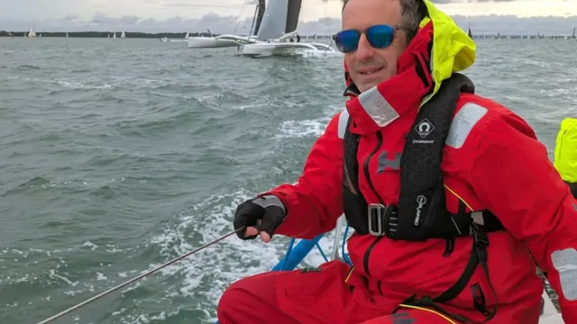 Sailing school student in red foul-weather gear trimming a line on a yacht
