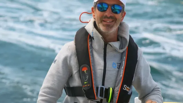 Sailing school student at the helm of a yacht wearing sunglasses and a white cap