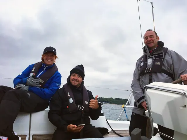 Sailing school students smiling together on deck, one at the helm of a yacht