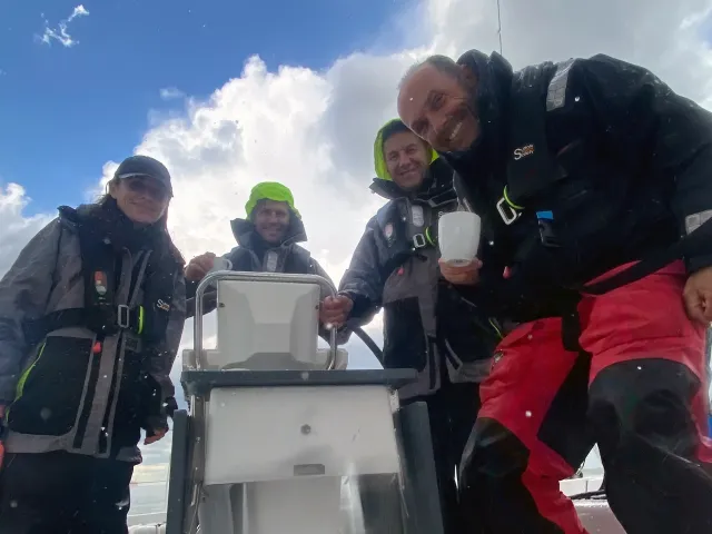 Crew members at the helm of a sailing school yacht in wet weather gear