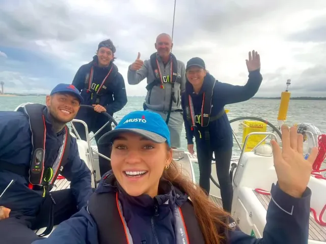 Sailing school students and instructor smiling and waving on deck during a training sail