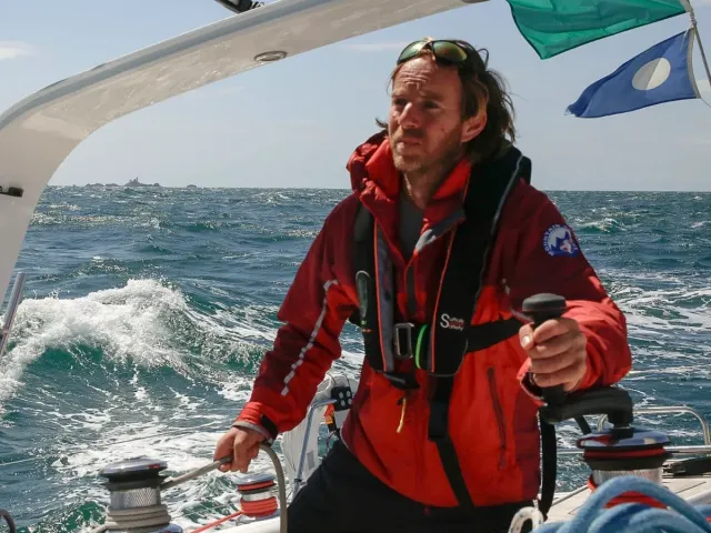 Sailing school student helming a yacht in rough seas wearing red foul-weather gear