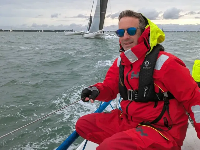 Sailing school student in red foul-weather gear trimming a line on a yacht