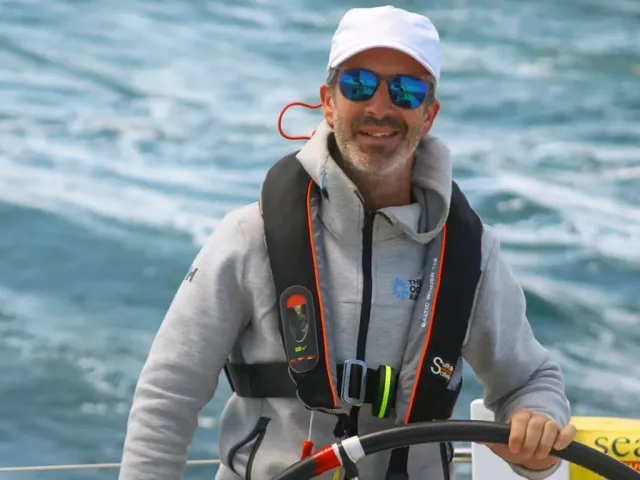 Sailing school student at the helm of a yacht wearing sunglasses and a white cap
