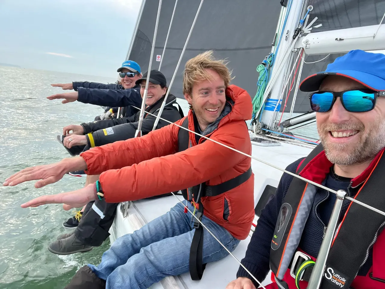 Sailing school students hiking out on the side of a yacht during training