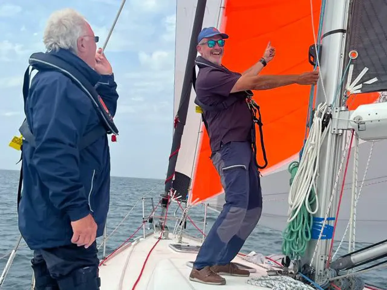 Sailing school instructor adjusting sails on a yacht with bright orange spinnaker