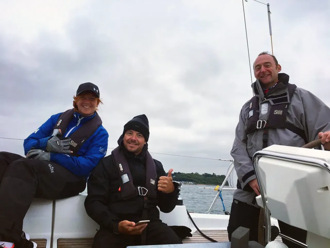 Sailing school students smiling together on deck, one at the helm of a yacht