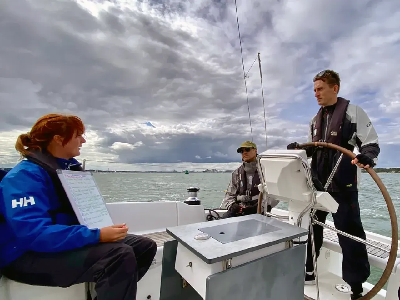 Sailing school students practising helming a yacht while making notes on a whiteboard