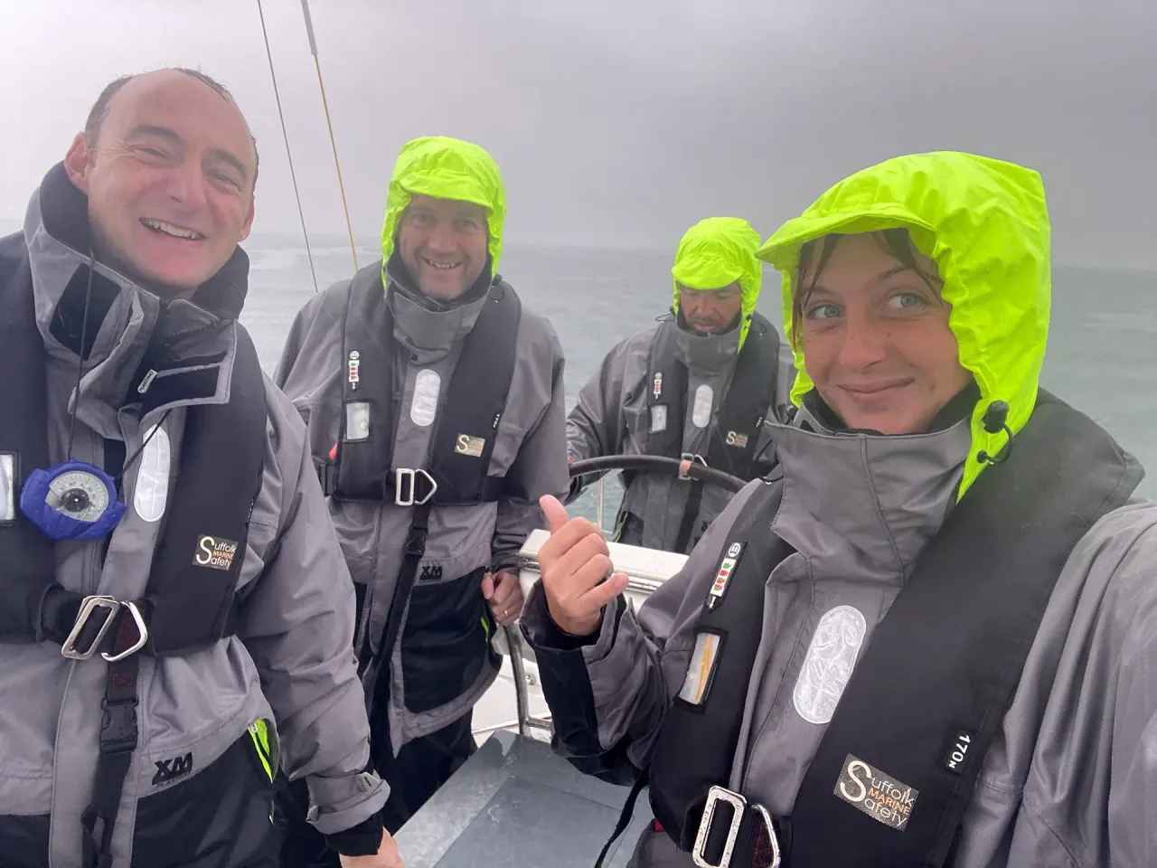 Sailing school students helming a yacht in heavy rain wearing grey and neon yellow foul-weather gear