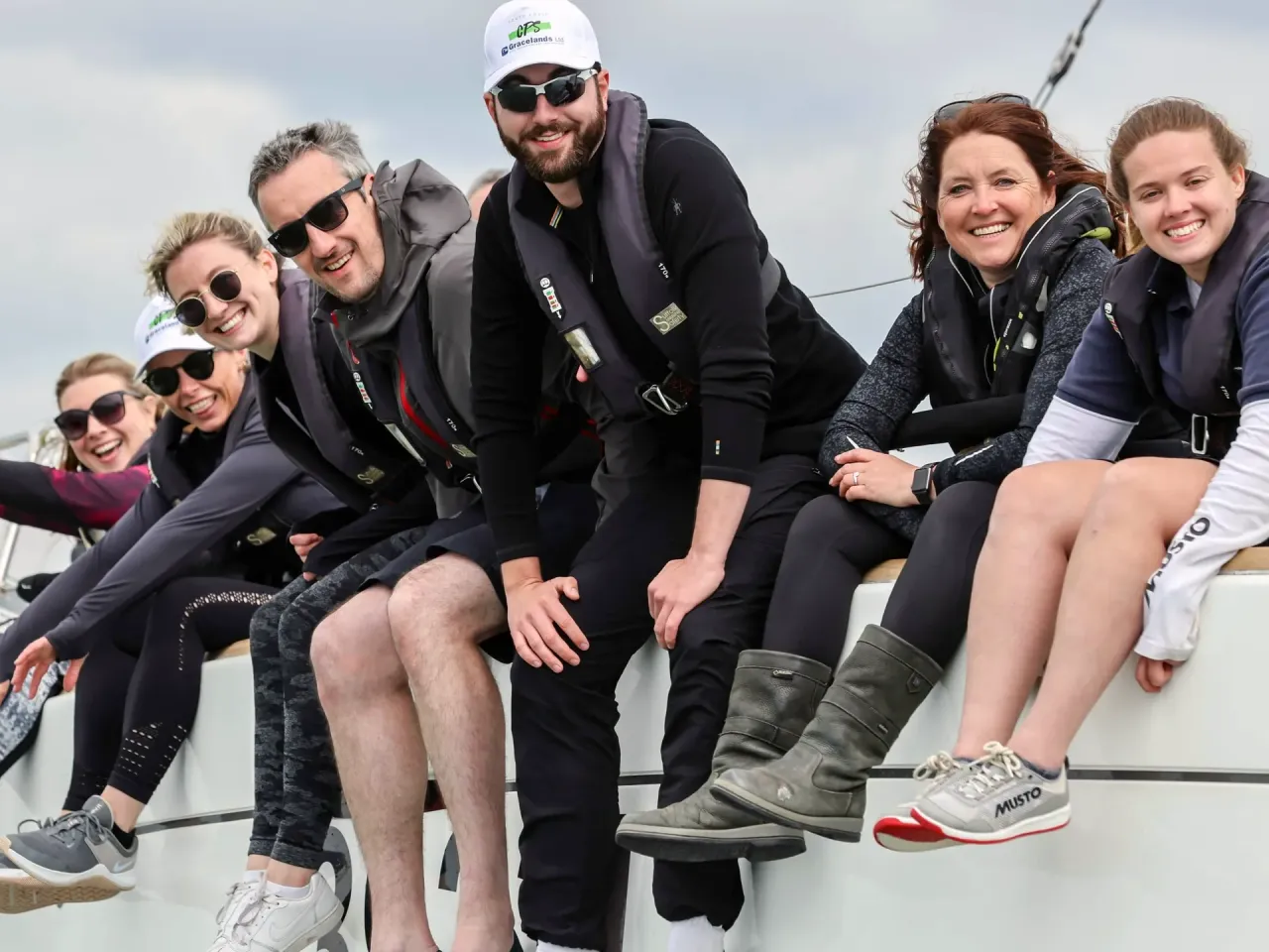 Group of sailing school students sitting on the rail of a yacht during training