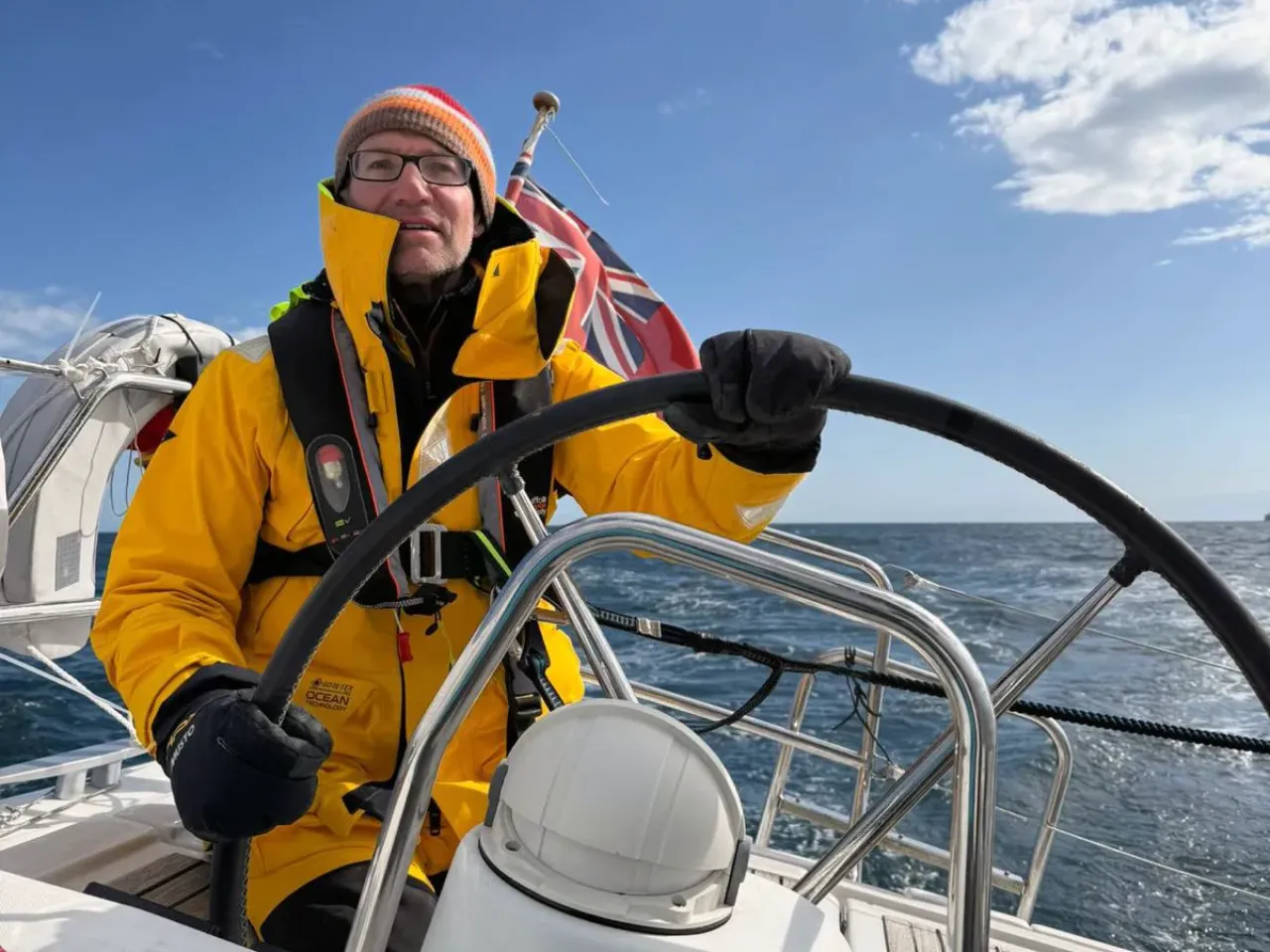 Sailing school student in yellow foul-weather gear steering a yacht at sea