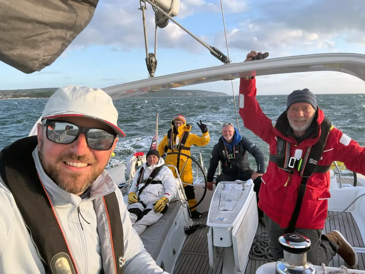 Sailing school crew and instructor smiling at the helm of a yacht in choppy seas